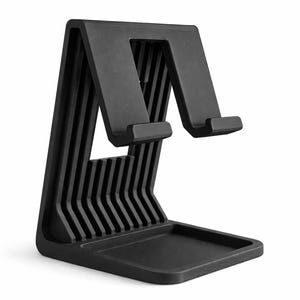 Könnte beinhalten: Schwarzer Telefonständer mit einzigartigem Design. Der Ständer hat eine Basis mit einer kleinen Ablage, eine vertikale Stütze mit parallelen Linien und eine abgewinkelte Oberseite mit zwei Vorsprüngen zur Aufnahme eines Telefons. Hergestellt aus mattem, schwarzem Material.