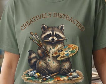 Creatively Distracted Raccoon Painter T-Shirt | Art Animal Illustration Neurodivergent Comfort Color Graphic Tee