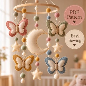May include: A hanging mobile featuring a central felt moon, four felt butterflies in pink, green, yellow, and blue, and felt stars suspended from a wooden ring. The mobile includes colorful felt balls and text reading PDF Pattern and Easy Sewing.