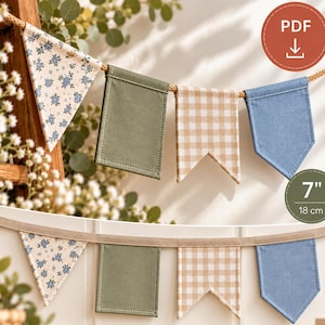 Puede incluir: Una guirnalda de tela con cuatro banderines distintos: uno triangular con estampado floral, uno rectangular verde oliva, uno con forma de cola de golondrina a cuadros beige y blancos, y una bandera azul pentagonal. Mide 18 cm de alto.