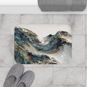 May include: A rectangular bath mat with a mountain landscape design in blue, brown, and white. The mat is on a tiled floor, with gray slippers below. A gray towel is in the background. The mat's design evokes a sense of nature.