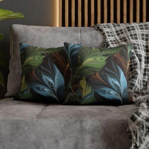 May include: Two rectangular throw pillows with a dark background and a colorful feather-like pattern in shades of blue, green, brown, and yellow. The pillows are resting on a gray sofa, with a plaid blanket visible.