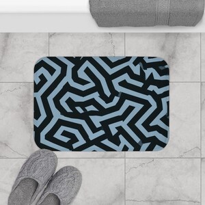 Peut inclure: Un tapis de bain rectangulaire arborant un motif géométrique audacieux en forme de labyrinthe, composé de nuances contrastées de noir charbon foncé et de bleu clair atténué. Le design présente des lignes épaisses entrelacées et continues.