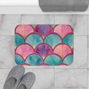 May include: A rectangular bath mat featuring a repeating fan-shaped pattern in shades of pink, purple, and teal. Each fan segment is outlined with thin gold lines, creating a geometric design across the entire surface of the mat.