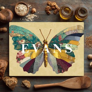 May include: A rectangular cutting board featuring a colorful butterfly design. The butterfly wings are composed of various patterned fabrics in teal, gold, red, and blue. The word "EVANS" is displayed across the center in white. The board is set on a wooden surface.