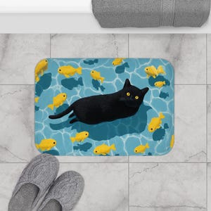 May include: A rectangular bath mat featuring a black cat floating in a pool of water with yellow fish. The water is a light blue color with darker blue shadows. The cat has yellow eyes and is lying down.