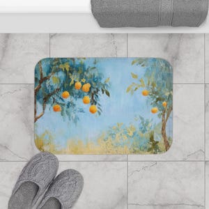 Op de afbeelding: Een rechthoekige badmat met een geschilderde scène van sinaasappelbomen met rijpe sinaasappels tegen een blauwe lucht. De mat heeft een afgeronde rand en ligt op een betegelde vloer. Grijze pantoffels staan onderaan.