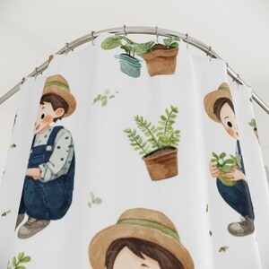 Puede incluir: Cortina de ducha blanca con un patrón de acuarela repetido de una persona con overoles y sombrero de paja, con plantas en macetas y hojas verdes. El diseño incluye abejas y pequeños acentos de hojas verdes.