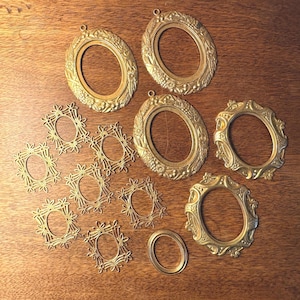 May include: A collection of antique gold-colored oval and floral picture frames. The frames vary in size and design, with some featuring intricate floral patterns and others with simpler, elegant lines. The frames are arranged on a wooden surface.