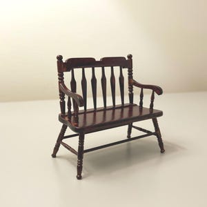 May include: A miniature wooden bench with a dark brown finish. The bench features a slatted back, armrests, and turned legs. This dollhouse furniture piece is a classic design.