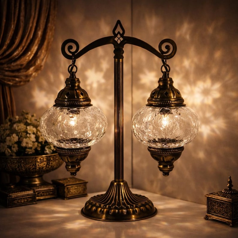 May include: A decorative table lamp featuring two crackled glass globe shades. The lamp has a bronze-coloured metal frame with a detailed base and a curved top. The illuminated shades cast a warm glow and intricate light patterns, creating a cosy atmosphere.
