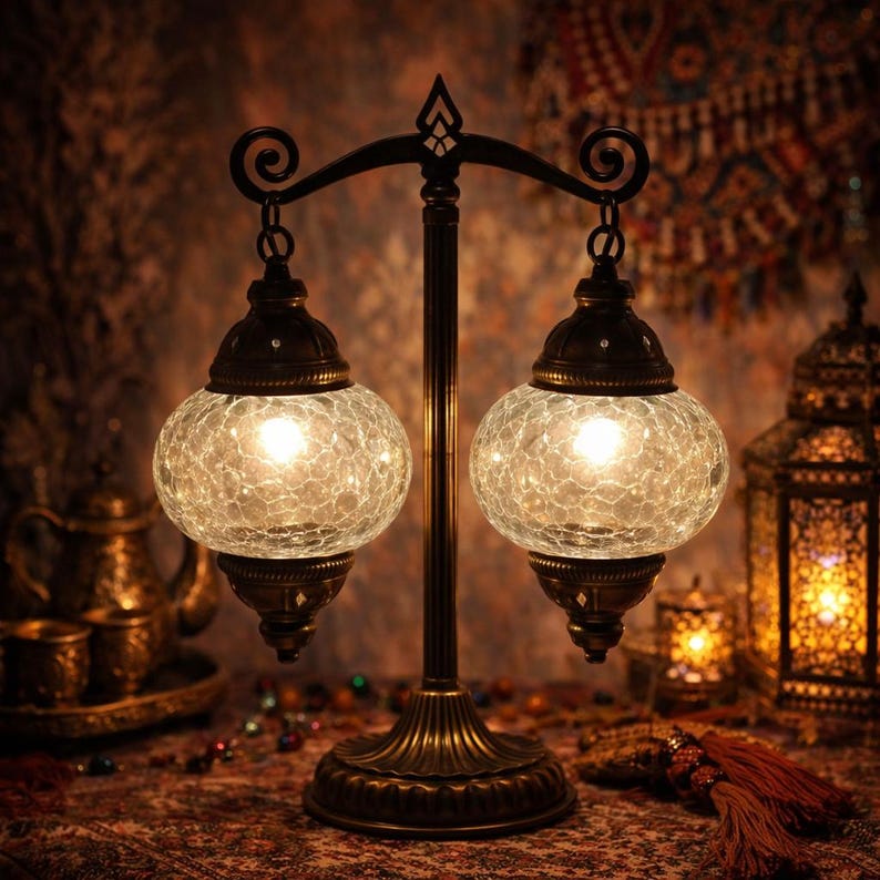 May include: A decorative table lamp featuring two spherical, crackled glass shades. The lamp has a bronze-coloured metal base and a curved top. The shades are illuminated, emitting a warm light. The lamp is designed in an ornate, vintage style.