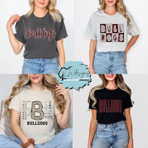 May include: Four t-shirts with the word "Bulldogs" in various designs. One shirt is dark gray with red script, another is light gray with the word in a block design, a third is tan with a leopard print "B", and the last is black with the word repeated.