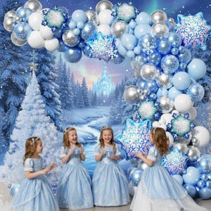 May include: A balloon arch featuring a mix of light blue, white, and silver balloons with large snowflake-shaped foil balloons. The arch is arranged in a curved design, creating a festive winter-themed display for a holiday celebration.