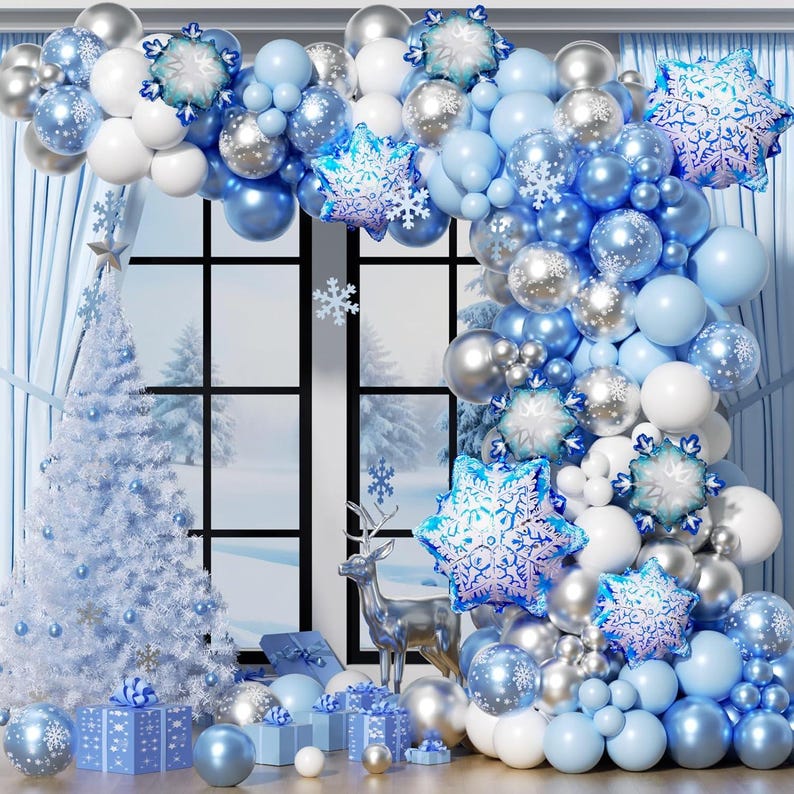 May include: A balloon arch featuring a mix of light blue, white, and metallic silver balloons, accented with large foil snowflake balloons. The arrangement is displayed around a window frame, accompanied by a white Christmas tree and gift boxes.