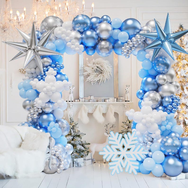 May include: A balloon arch kit featuring a mix of metallic blue, silver, and matte white balloons. The display includes large silver and blue star-shaped foil balloons, white snowflake-shaped balloon clusters, and a large white snowflake cutout.