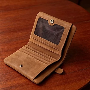 May include: Open, brown leather wallet with multiple card slots and a clear ID window. The wallet is secured with a snap closure and features a classic, minimalist design. The wallet is made of a textured leather material.