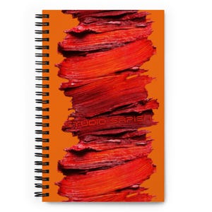 Puede incluir: Cuaderno de espiral con una cubierta naranja vibrante que presenta un diseño audaz de pinceladas rojas en capas. El texto "studio sapier" está impreso en rojo en el centro del diseño. El cuaderno tiene una encuadernación en espiral negra.
