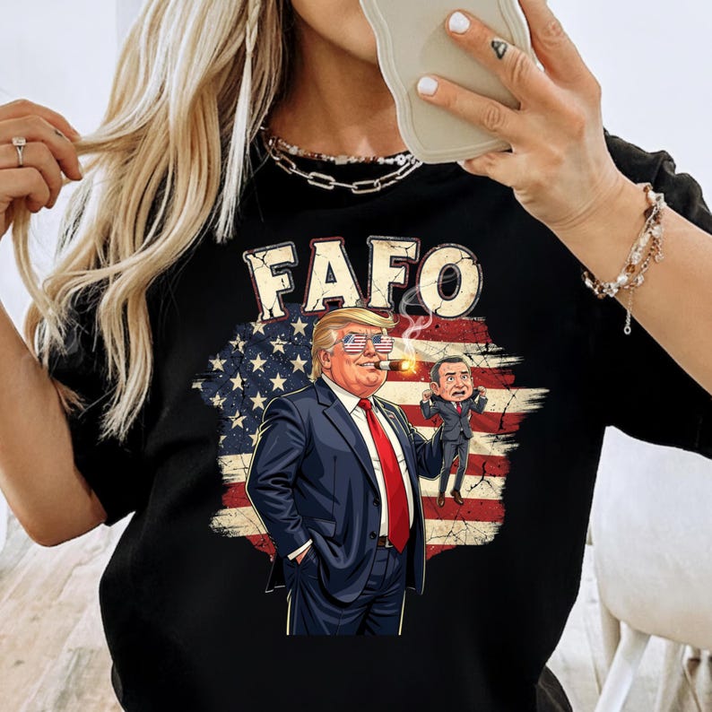 May include: Black t-shirt with the word "FAFO" above a graphic of a man in a suit wearing sunglasses and smoking a cigar, with a smaller figure next to him, set against a distressed American flag background.