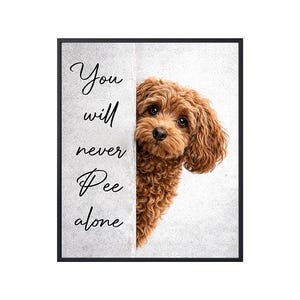 May include: Framed wall art featuring a brown poodle peeking from behind a white panel. The text "You will never Pee alone" is written in black script on the panel. The artwork has a black frame.