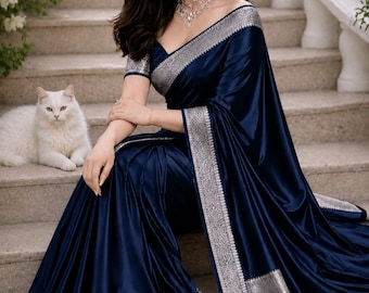 May include: A deep navy blue satin saree featuring a wide, intricate silver metallic border with detailed floral patterns. The garment includes a matching short-sleeved blouse and a long, flowing drape that pools on the stone steps beside a white cat.