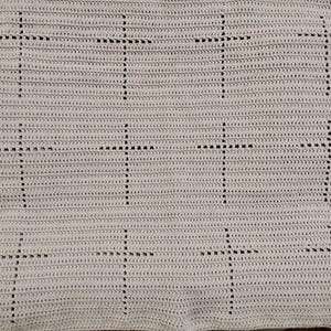 May include: Cream-coloured crocheted blanket with a repeating pattern of black crosses. The blanket is made from a soft, textured yarn, and the crosses are evenly spaced. The design is simple and elegant, suitable for a variety of uses.