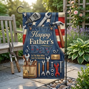 Puede incluir: Una bandera de jardín con un diseño de delantal de mezclilla, con herramientas y el texto "Happy Father's Day". La bandera tiene un fondo de bandera estadounidense e incluye llaves, un martillo y una cinta métrica. La bandera se muestra al aire libre.