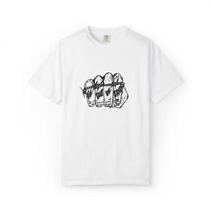 May include: White t-shirt with a black graphic of a clenched fist. The knuckles are labeled "THE", "POUR", "OF", and "GRACE". The design is a bold, illustrative style. The shirt has a crew neck and short sleeves.