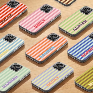 Puede incluir: Una colección de fundas para teléfonos inteligentes con patrones de rayas coloridas y nombres personalizados. Las fundas presentan una variedad de colores, incluyendo rojo, rosa, naranja, verde, azul y amarillo. Cada funda tiene un nombre diferente impreso.