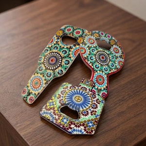 Peut inclure: Deux ouvre-bouteilles décoratifs avec des motifs de mosaïque colorés. L'un est en forme de clé, l'autre rectangulaire. Les motifs comprennent des formes géométriques bleues, vertes, rouges et jaunes. Ils sont en matériau brillant, sur une surface en bois.