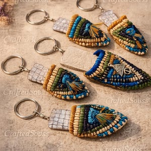 Peut inclure: Plusieurs porte-clés faits à la main avec un motif tissé bleu, vert et beige. Chaque porte-clés a un anneau argenté et une étiquette rectangulaire. Certains ont un petit charme en métal.
