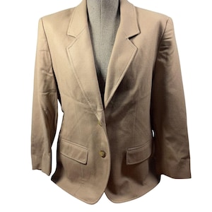 Puede incluir: Un blazer de color tostado sólido con solapa de muesca, mangas largas y cierre frontal de dos botones. La prenda incluye dos bolsillos horizontales con solapa situados en la cintura y hombros estructurados, presentando un aspecto uniforme.