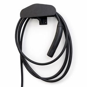 Puede incluir: Un cable y conector de carga para vehículos eléctricos de color negro, enrollado y colgado de un soporte de pared negro. El soporte tiene una parte superior triangular y un soporte para el montaje. El cable es grueso y flexible.