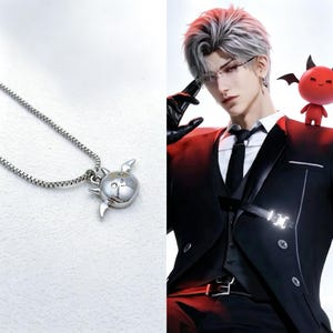 Può includere: Una collana in metallo color argento con un piccolo ciondolo arrotondato a forma di creatura stilizzata con due orecchie a punta e due piccole ali sui lati. Il ciondolo è fissato a una sottile catena a maglie quadrate con finitura lucida.