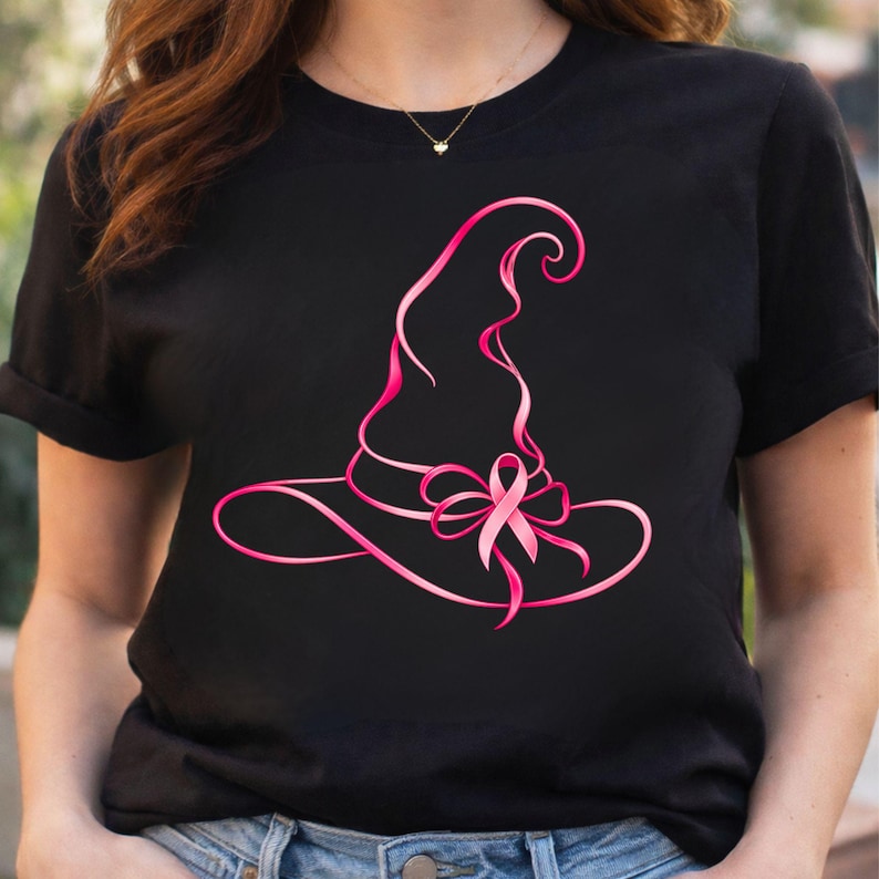 May include: A black short-sleeved t-shirt featuring a graphic design of a witch hat outlined in a vibrant pink ribbon. The ribbon forms the shape of the hat and includes a prominent pink awareness ribbon bow tied at the base of the hat's crown.