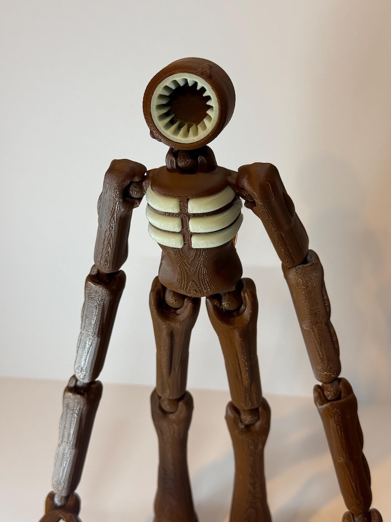 May include: A brown articulated figure with a siren-like head and a ribcage design. The figure has a circular head with a white interior, brown arms and legs, and a light-colored ribcage. The figure is a unique, detailed design.