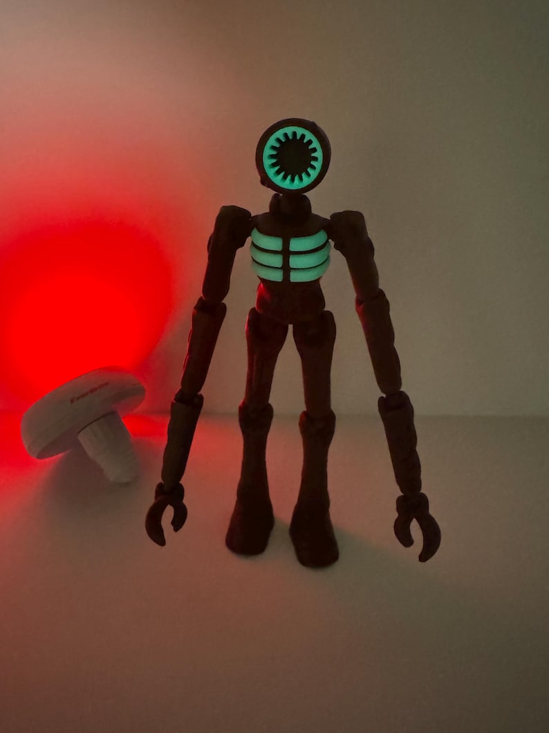 May include: A brown action figure with a siren-shaped head and glowing green details on the head and chest. The figure has articulated limbs and stands upright. A white mushroom-shaped object is in the background.