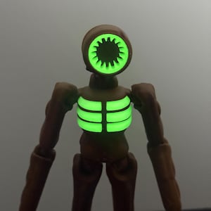 May include: A brown action figure with a unique design. The figure has a head shaped like a speaker with a glowing green interior. The chest also glows green. The figure has articulated limbs and a minimalist aesthetic.