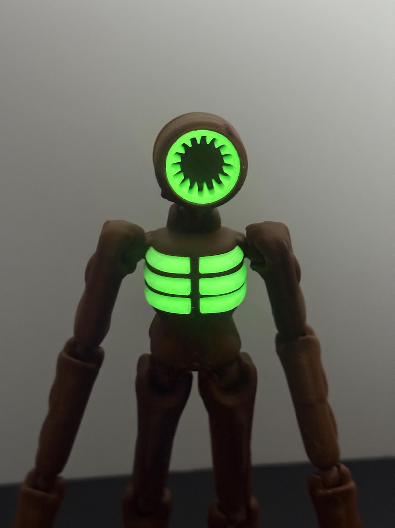 May include: A brown action figure with a unique design. The figure has a head shaped like a speaker with a glowing green interior. The chest also glows green. The figure has articulated limbs and a minimalist aesthetic.