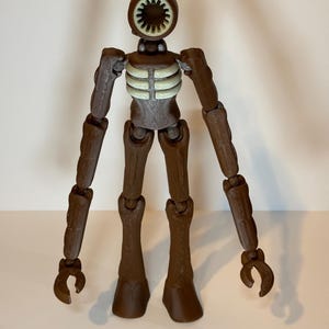 May include: A brown articulated figure with a circular head featuring a speaker-like design. The figure has a skeletal chest and long, jointed limbs ending in claw-like hands and feet. The figure is standing against a plain background.