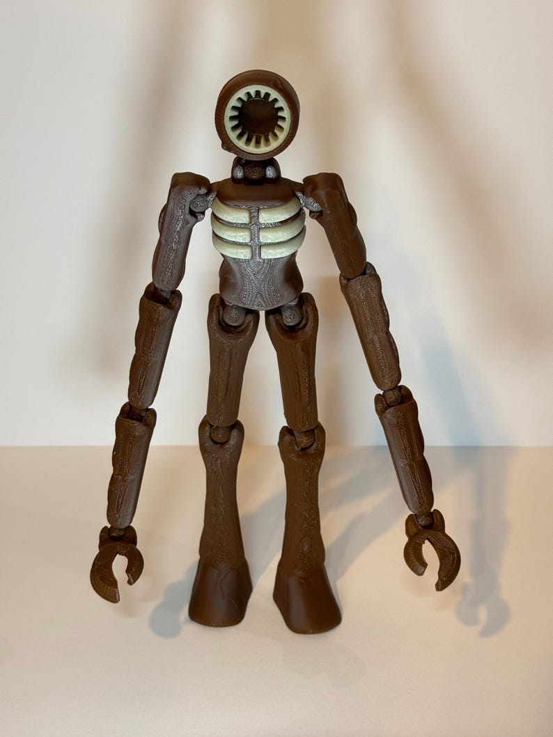 May include: A brown articulated figure with a circular head featuring a speaker-like design. The figure has a skeletal chest and long, jointed limbs ending in claw-like hands and feet. The figure is standing against a plain background.