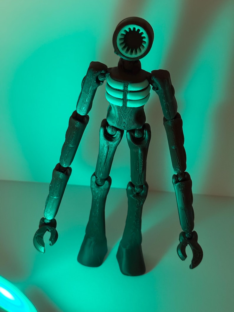 May include: A dark green articulated figure with a circular head featuring a speaker-like design. The figure has a ribcage detail and claw-like hands. The figure is standing in front of a green background.
