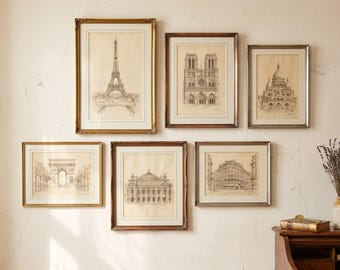 May include: A collection of framed architectural sketches of Parisian landmarks, including the Eiffel Tower, Notre Dame Cathedral, and the Arc de Triomphe. The sketches are in black and white, with gold and brown frames, displayed on a cream-colored wall.