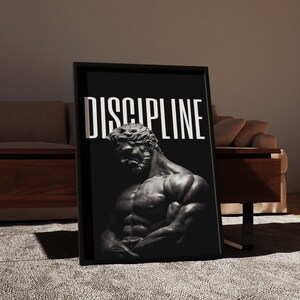 May include: Black framed wall art featuring a grayscale image of a muscular male statue. The word "DISCIPLINE" is printed in white block letters above the statue. The artwork is displayed in a room with a neutral color palette.