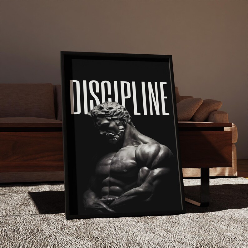 May include: Black framed wall art featuring a grayscale image of a muscular male statue. The word "DISCIPLINE" is printed in white block letters above the statue. The artwork is displayed in a room with a neutral color palette.
