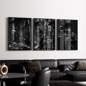 Könnte beinhalten: Ein Triptychon gerahmter Schwarz-Weiß-Stadtlandschaften. Die Bilder zeigen nächtliche urbane Szenen mit beleuchteten Wolkenkratzern, Straßen und Verkehr. Das Kunstwerk wird über einem schwarzen Ledersofa präsentiert.