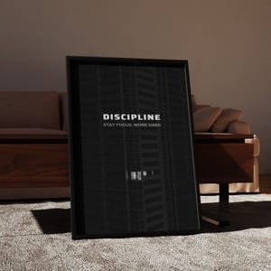 May include: A framed black print with the word "DISCIPLINE" in white, along with the text "STAY FOCUS, WORK HARD." The image inside the frame depicts a dark, abstract skyscraper. The frame is leaning against a wall.