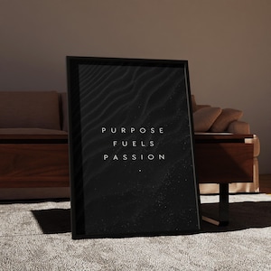 May include: A framed black and white art print with the words "PURPOSE FUELS PASSION" in white lettering. The artwork features a textured, abstract design. The frame is black and the print is displayed on a neutral-colored rug.
