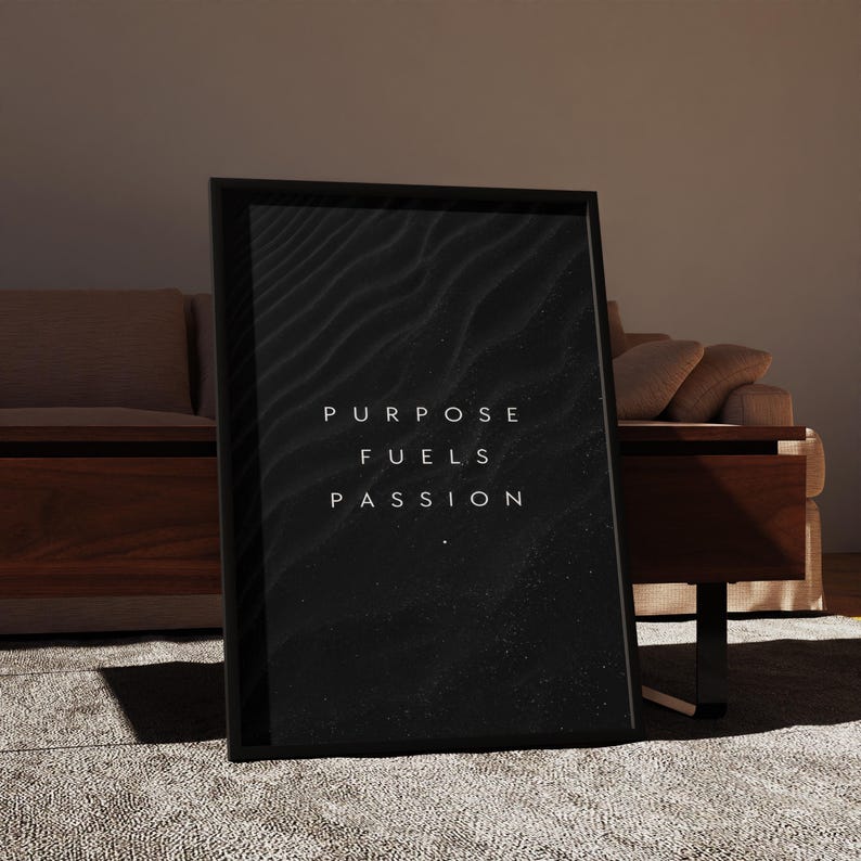 May include: A framed black and white art print with the words "PURPOSE FUELS PASSION" in white lettering. The artwork features a textured, abstract design. The frame is black and the print is displayed on a neutral-colored rug.
