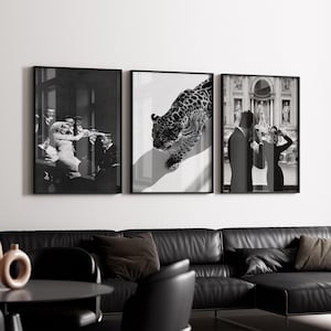 May include: Set of three framed black and white art prints. The prints depict a vintage scene, a leopard, and a couple in front of a building. The prints are displayed above a black leather sofa.